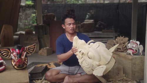 Wood Carver Blowing The Dust Off On Barong Bangkal Mask, Mythical Animal That Has Strength. - close