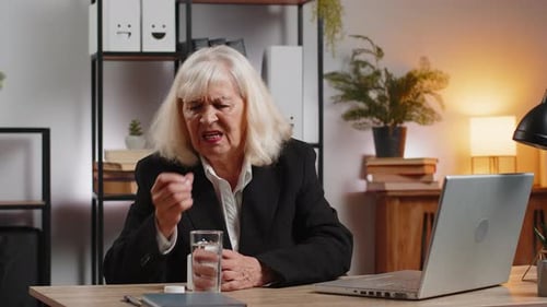 Senior Woman Taking Medicine at Desk in Office