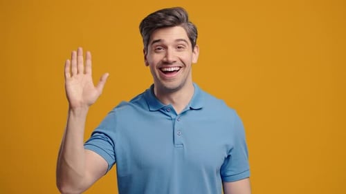Friendly American Mature 30s Aged Man Waving Hand Hello Hi Salute Chao Greetings on Yellow Studio
