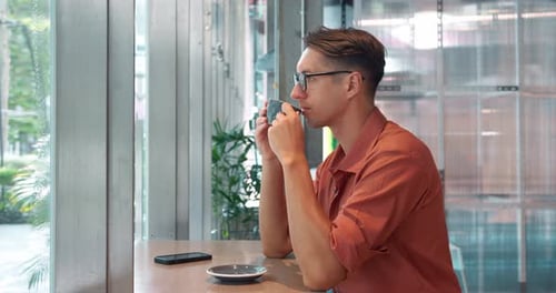 Pensive Man with Glasses Sits in Cafe and Enjoys Cup of Delicious Hot Coffee Man Entered Cafe to