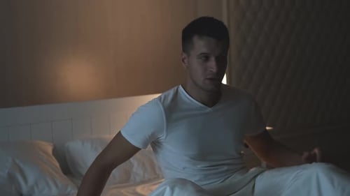 Vue de face d'un jeune homme caucasien choqué qui dort trop longtemps et se lève rapidement alors qu'il est couché dans son lit.
