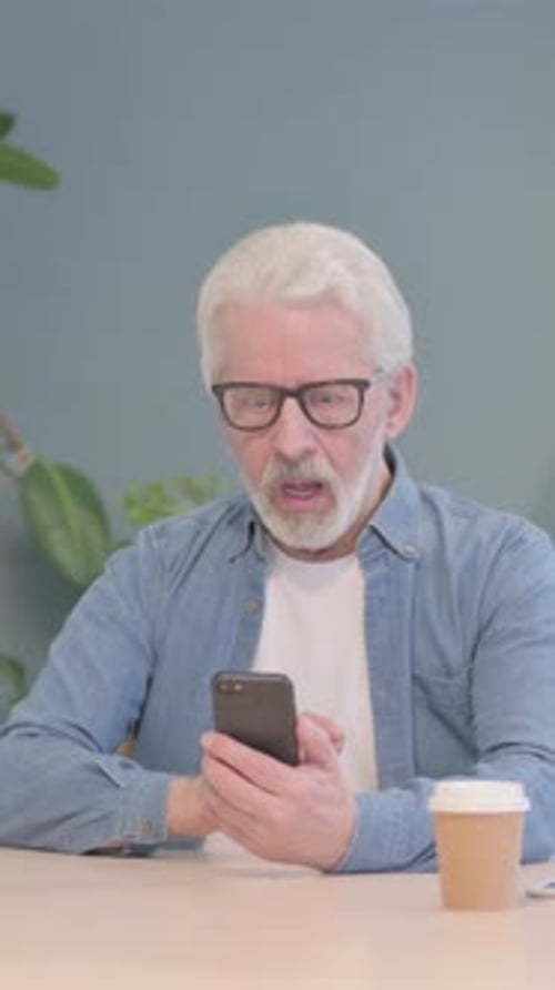 Senior Man Uses Smartphone at Desk Indoors