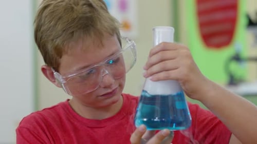 Young caucasian boy smiles at bubbling science experiment in school classroom