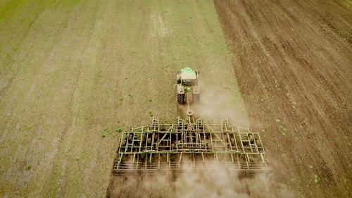 Large Green Tractor with Wide Cultivator Plowing Soil on Field for Removing Weeds From Ground