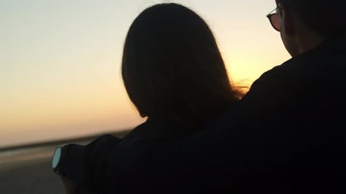 Couple watching the sunset and hugging at the beach, handheld close up