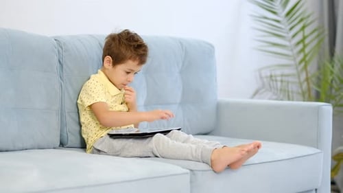 Preschool Boy Using Tablet Computer for Online Education Sitting on Couch at Home