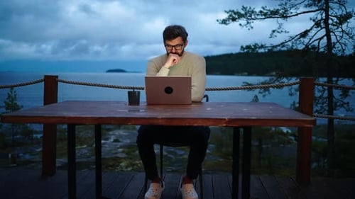 Mann arbeitet nachts mit Laptop und sitzt alleine auf der offenen Terrasse des Öko-Hotels