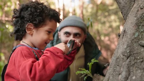 Enfant curieux explorant la nature avec une loupe et son père à l'extérieur