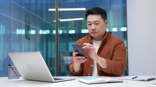 Asian businessman is using browsing mobile phone while sitting at workplace in business office.