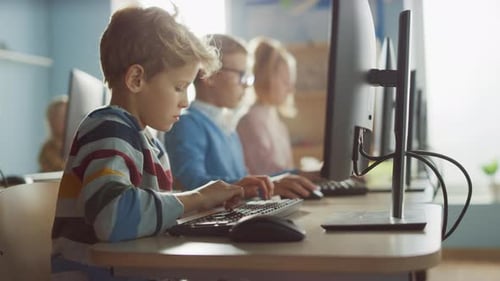 Elementary School Computer Science Classroom: Smart Little Boy Uses Personal Computer, Learning How