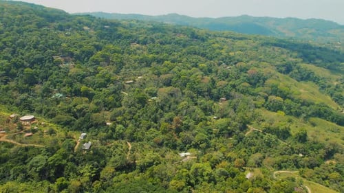 Aerial of rural tropical hillside with scattered houses among dense green forest