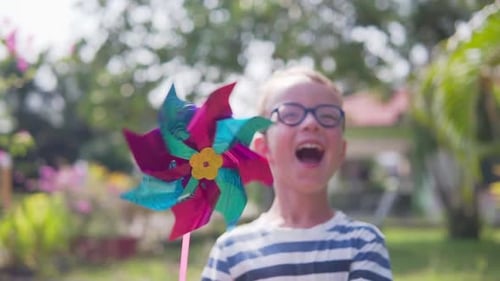 Boy in glasses is playing with pinwheel in a garden