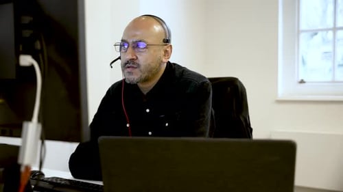 Empresario centrado en el sur de Asia hablando con auriculares en una oficina moderna