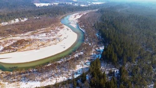 Aerial view of a winding river with sandy banks flowing through a winter forest landscape, partially