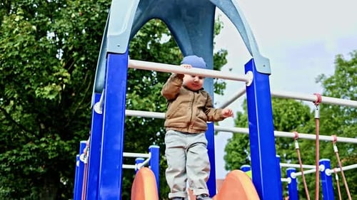 Little 2 year old boy slides down a slide on a playground. The boy has fun and plays on a playground