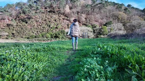 Traveler walking through green rural meadow surrounded by forested hills