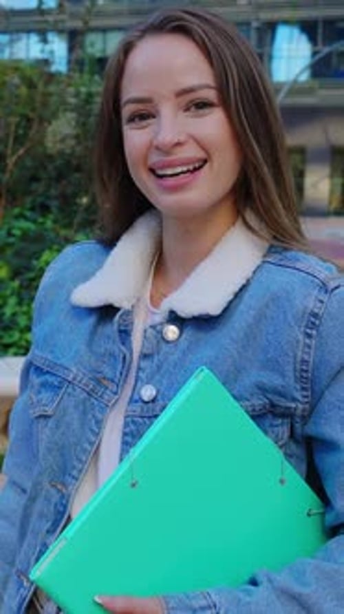 Smiling College Student Holding a Binder on Campus with Friends in Background
