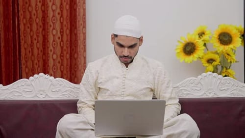 Homme musulman sérieux assis sur un canapé et travaillant sur un ordinateur portable