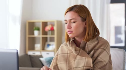 Woman Feeling Unwell, Sitting Indoors, Wrapped in Blanket