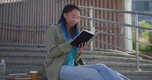 Woman Reads Book on Urban Steps in Daylight