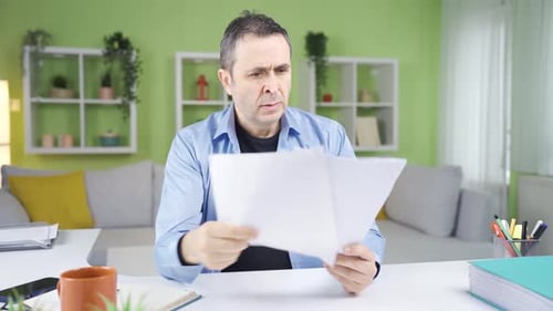 Frustrated Man Sitting at Desk Reviewing Paperwork