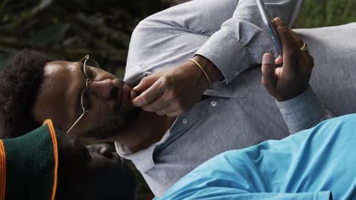 Man with Phone Lying in Nature with Friend