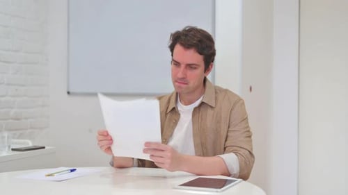 Man Reads Documents at Table and Smiles