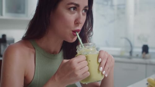 Woman Drinks Green Smoothie in Kitchen