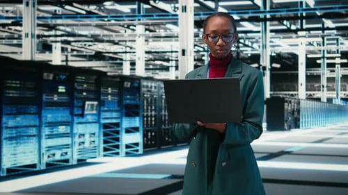 Managing Databases Laptop and Female Technician Walking in Data Center