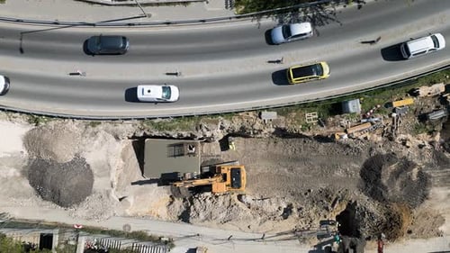 Luftaufnahme einer Straßenbaustelle mit Baggern, Lastwagen, Schotterhaufen und nahegelegenem Verkehr auf einem