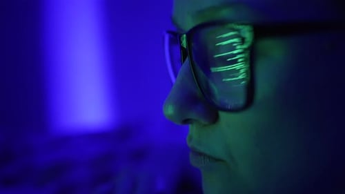 Une programmeuse de profil avec des lunettes regarde un écran d'ordinateur sur un fond bleu Programme vert