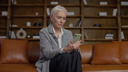 Senior Woman Using Smartphone on Brown Leather Couch