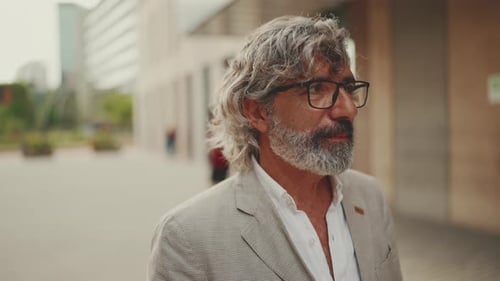 Clouse up mature businessman wearing gray jacket walks down the street past modern buildings