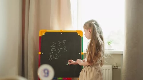 Girl Writes Answer on Blackboard Younger Child Shows Digit