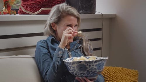 Dolly in of a young caucasian woman watching TV at home while eating chips and laughing at something
