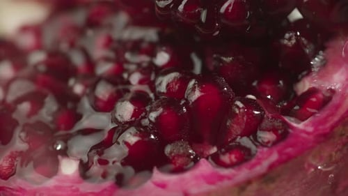 Gotas de agua que gotean sobre una granada en cámara lenta en macrosemillas de granate rojo de cerca