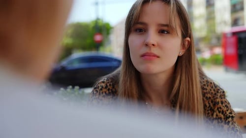 Relaxed Young Woman Drinking Coffee at Sidewalk Cafe Engaging in Intimate Conversation with Female