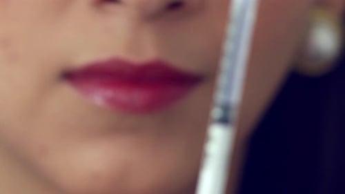 Filling a syringe from a vial - close up with rack focus to the face of the doctor