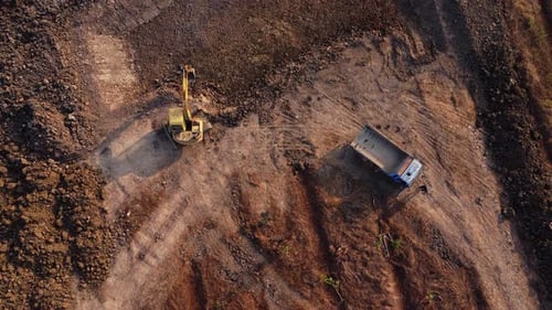 Aerial view of a wheel loader excavator with a backhoe loading sand into a heavy earthmover