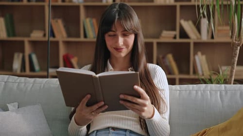 Young Woman Reads a Book on Couch