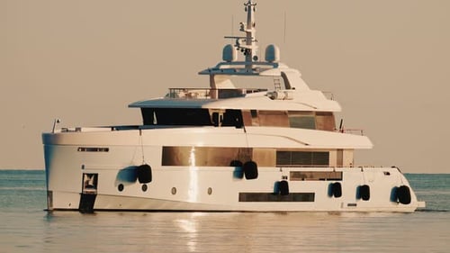 Side view of a modern luxury yacht moving across calm sea water with a lighthouse in the distance