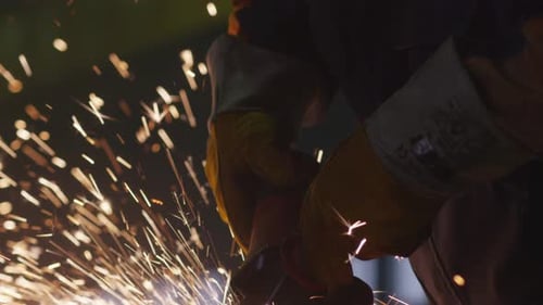 Schwerindustriearbeiter in einer Fabrik arbeitet mit Metall auf einem Winkelschleifer, während heiße Funken pr