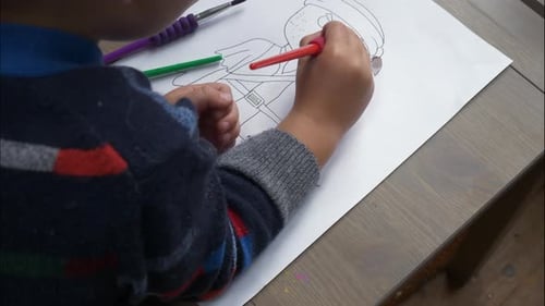 An over the shoulder, mid shot, timelapse of a small boy colouring in pirate figures with watercolou