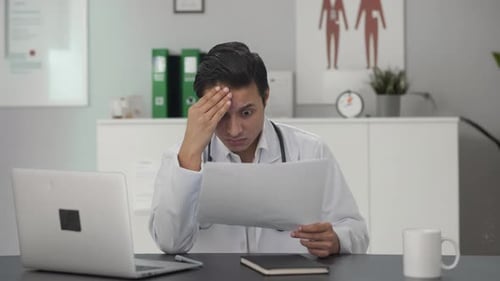 Worried Doctor Reading Medical Records in Office
