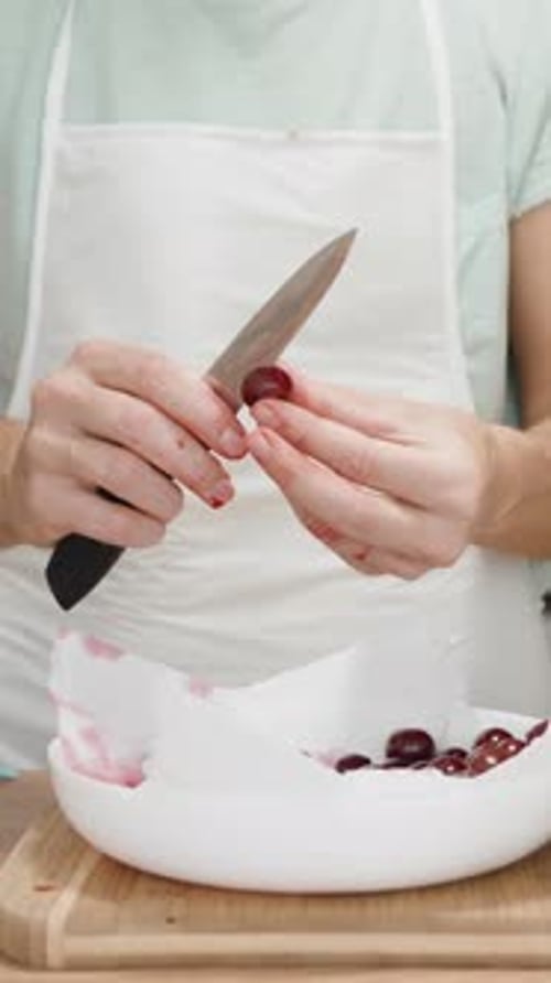 Verticale. La femme au tablier blanc a les mains rouges à cause du jus de cerise. Elle est en train de retirer les noyaux