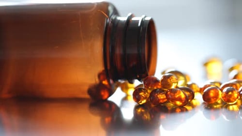 Pills spilling from bottle on reflective surface