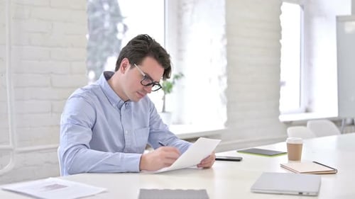 Serious Working Young Man doing Paperwork in Office