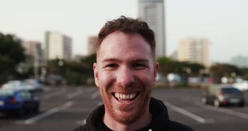 Young man smiling on camera outdoor with city street in background
