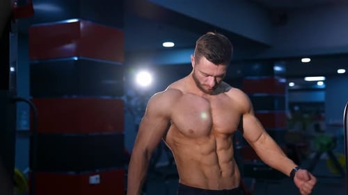 Muscular Man Posing Shirtless in Dark Gym