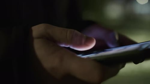 Hände einer Person, die nachts eine Nachricht auf einem Smartphone eingeben